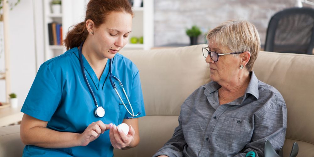 Nurse in nursing home helping senior woman with her pills.