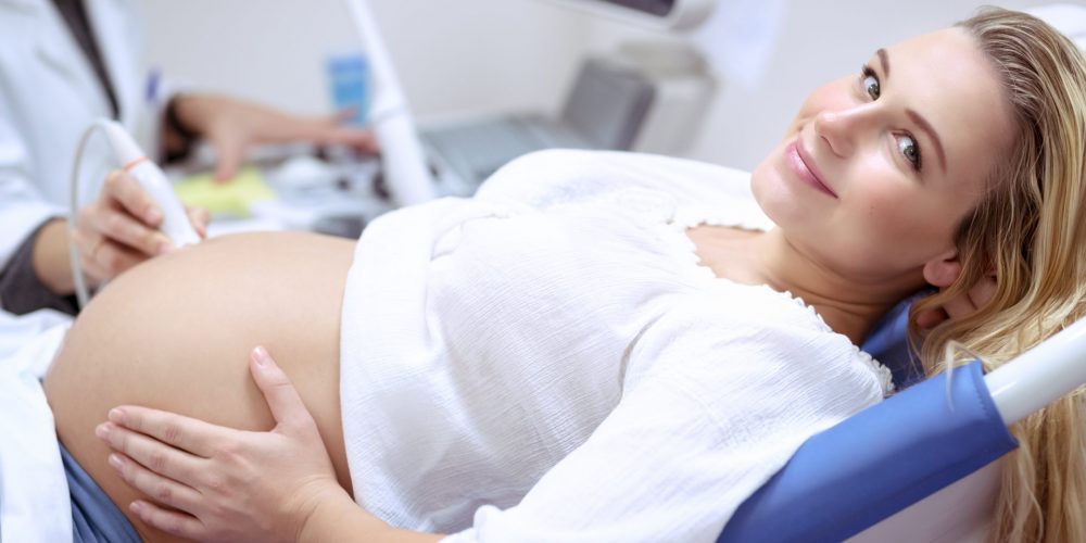 Happy pregnant female visiting women's doctor in the maternity center, with pleasure doing ultrasound scan, checking health of the child, healthy motherhood concept