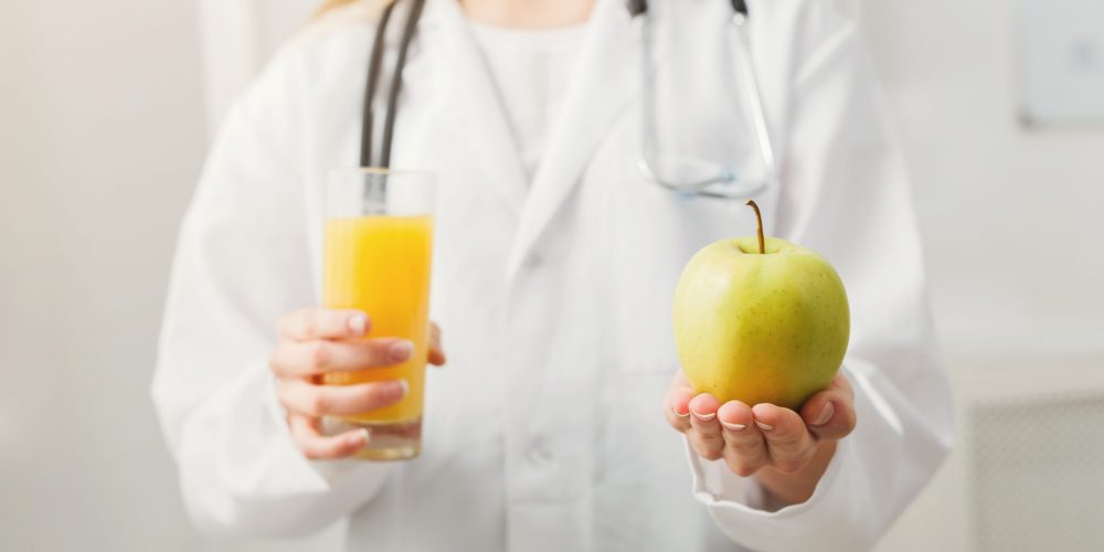 Unrecognizable nutritionist woman with orange juice and apple at office, copy space. Healthy eating, right nutrition and slimming concept